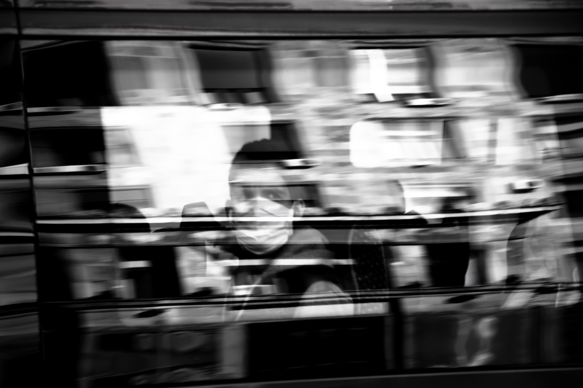 Blurry person wearing face surgical mask riding on a window seat of a public, in black and white with reflections